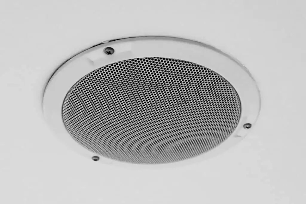 White round circle speaker and grille hanging on white ceiling. Selective focus